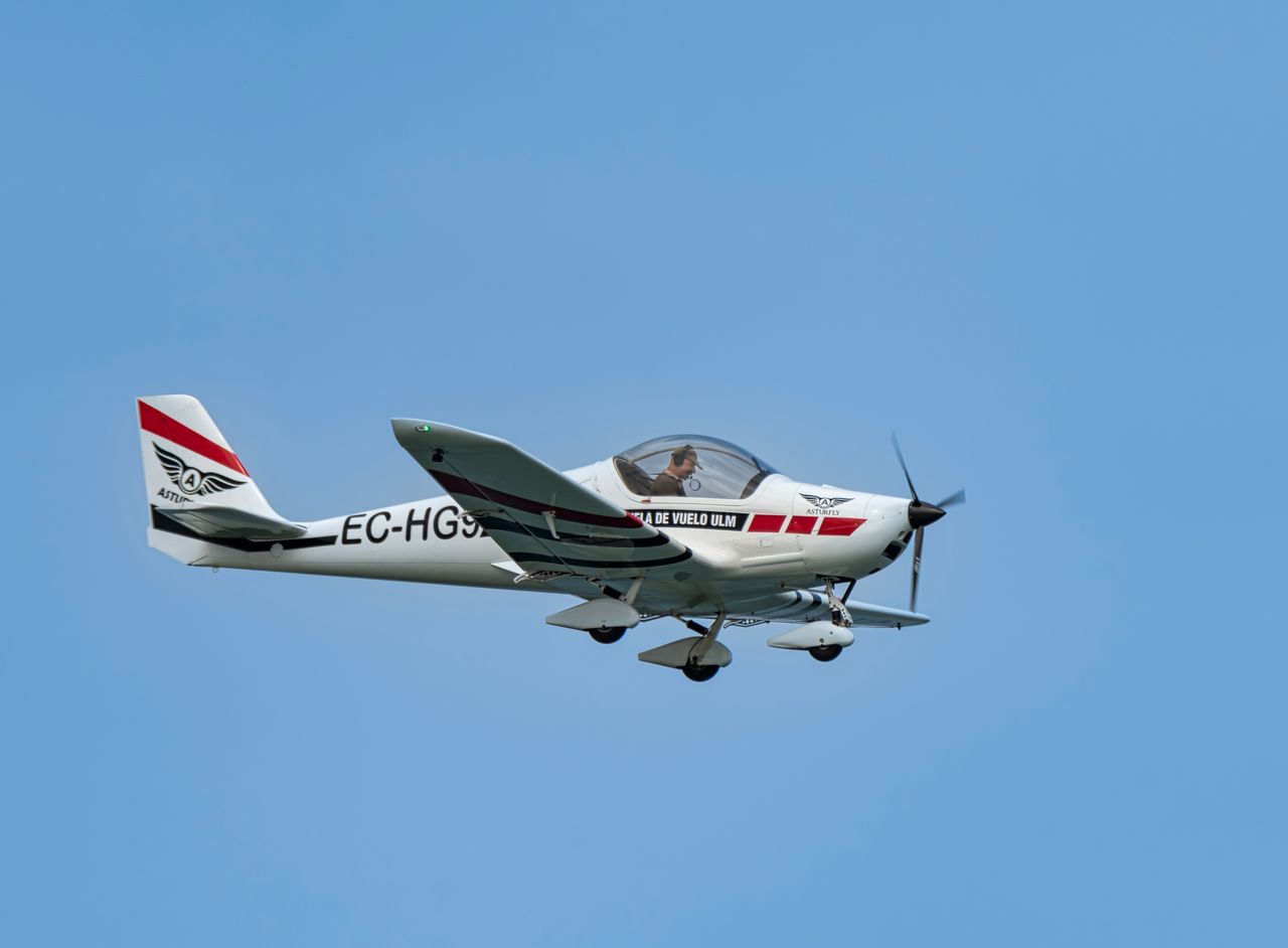 A small single-engine propeller aircraft flying with clear blue sky background.