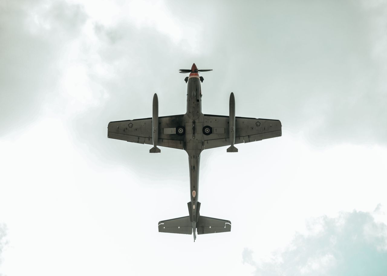 Aerial perspective of a plane flying overhead with clouds in the background.